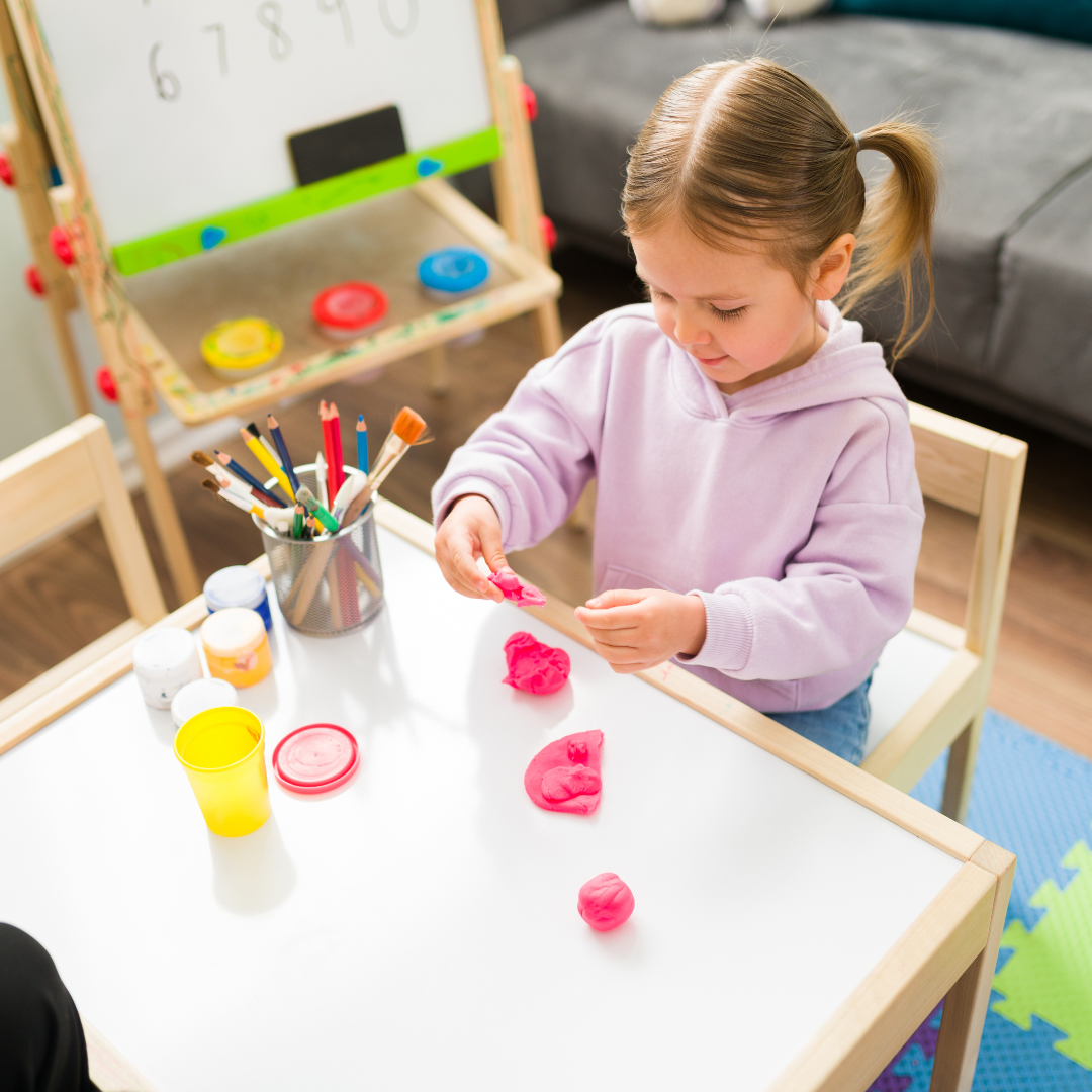 Young girl engaging in occupational therapy activities with pink playdough at a white table, developing fine motor skills.
